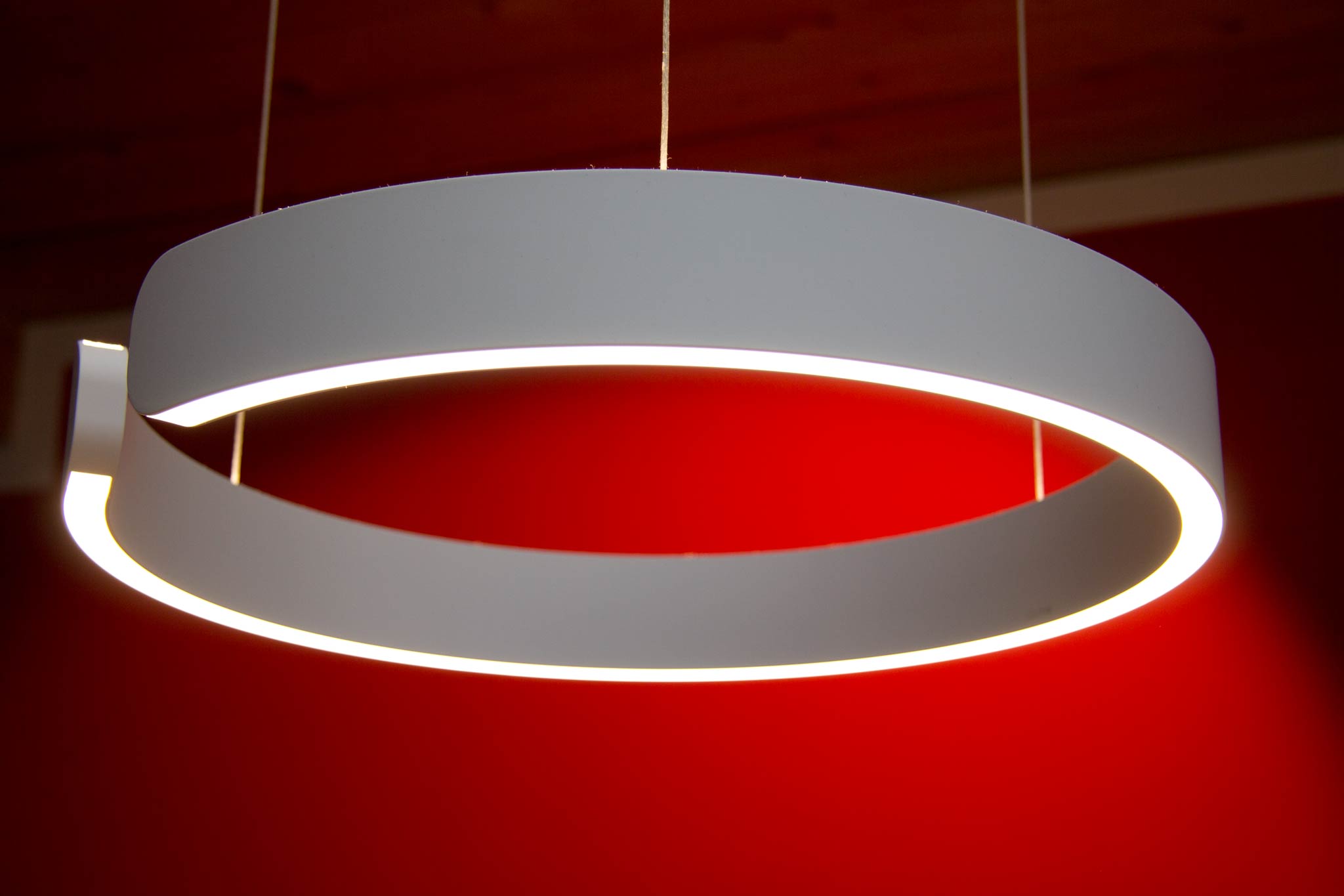 Eine moderne, weiße Esszimmerleuchte vom Hersteller Occhio. Die runde Leuchte ist nur an einer Stelle unterbrochen. Sie leuchtet nach oben und unten uns lässt sich mit Gesten dimmen und die Lichtfarbe steuern.