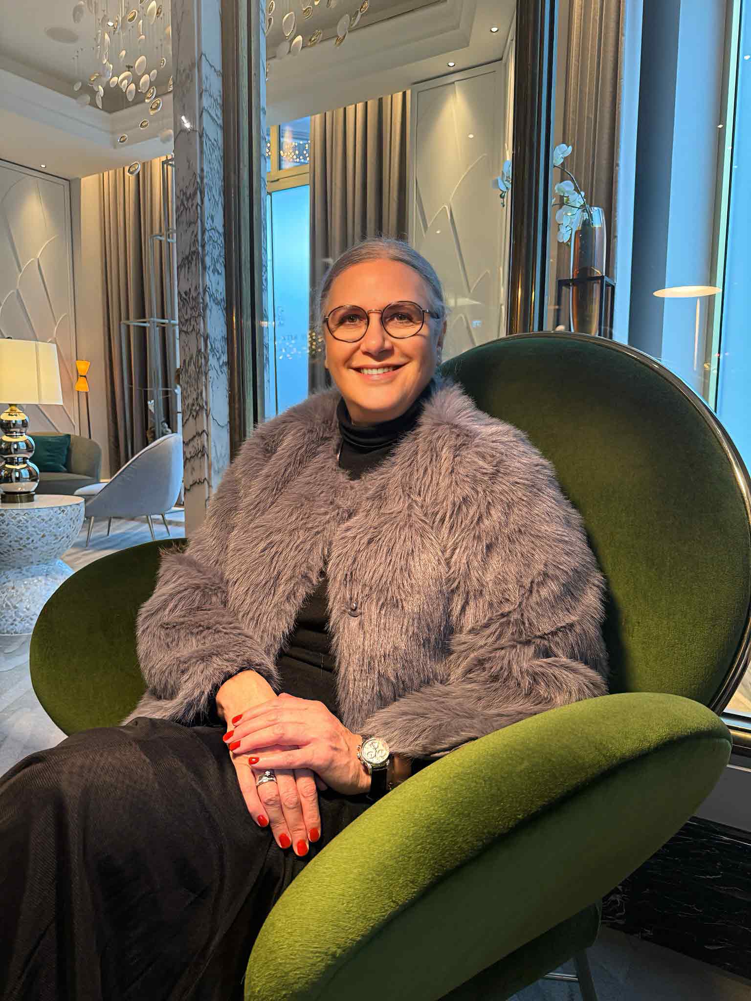 Jasminka Hepperle sitzt in einem modernen grünen Sessel. Der gesamte Raum einer Hotellobby ist entsprechend Grundsätzen von Interior Design gestaltet und wirkt sehr wohnlich und gemütlich.